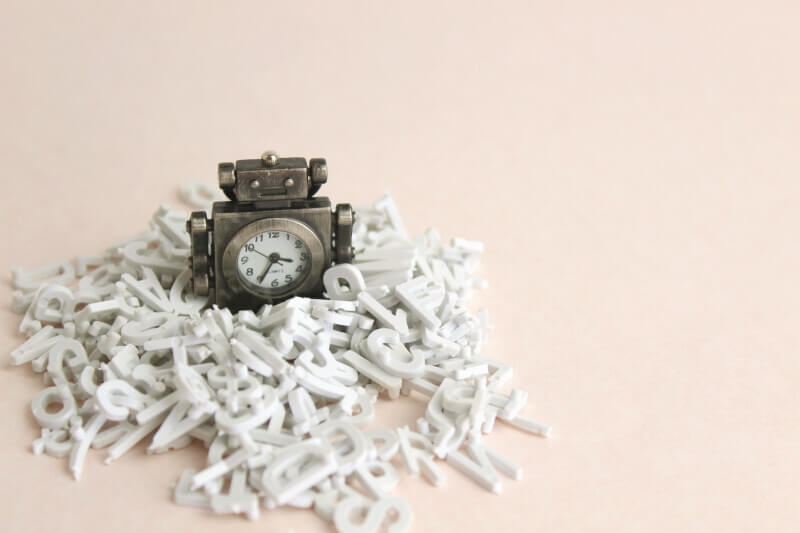 Miniature robot figure with a clock buried in a heap of letters