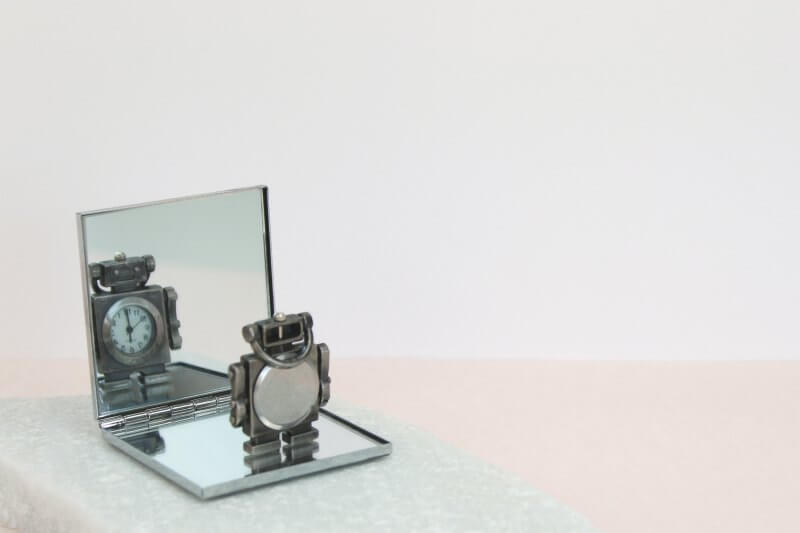 Miniature robot figure standing on a little compact mirror