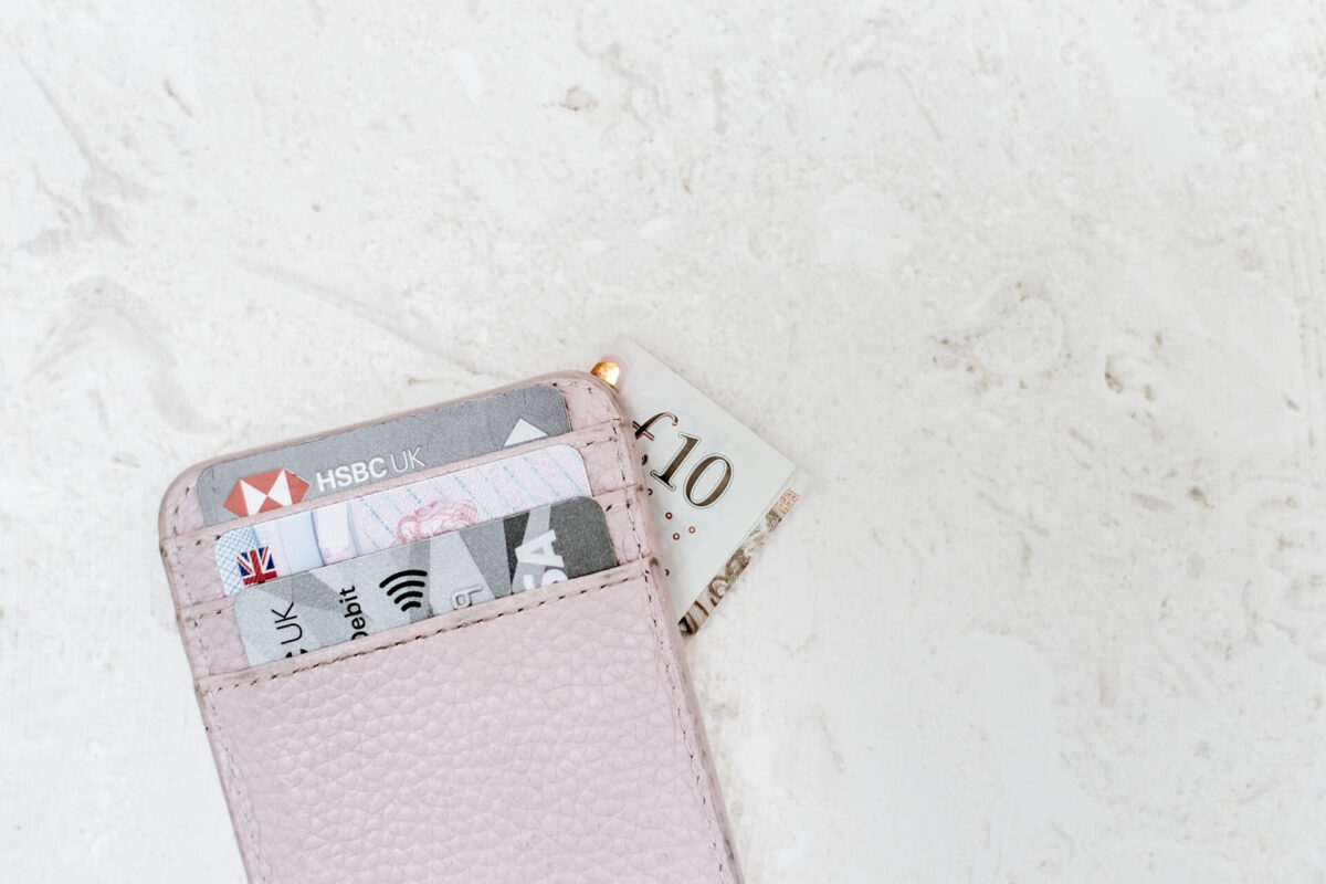 A pink textured leather card wallet with bank cards and a £10 note on a white marbled background.