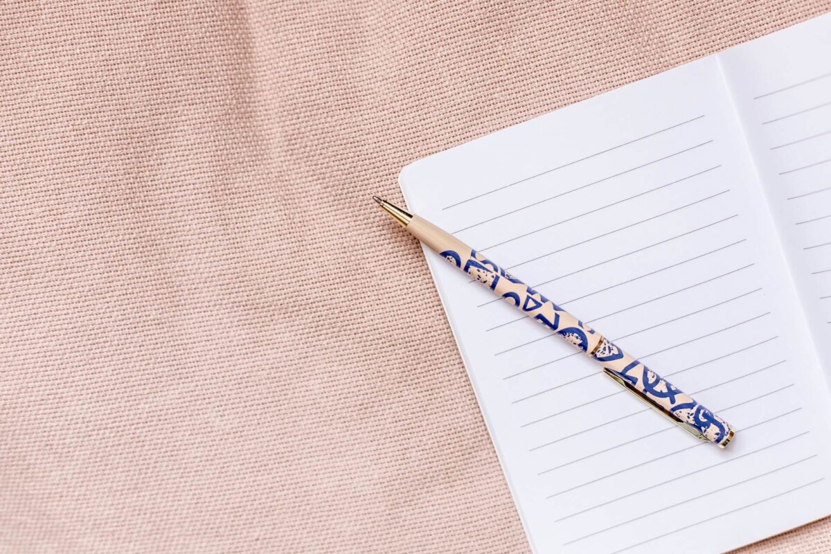 An open notebook with a pink pen on a pink fabric background.