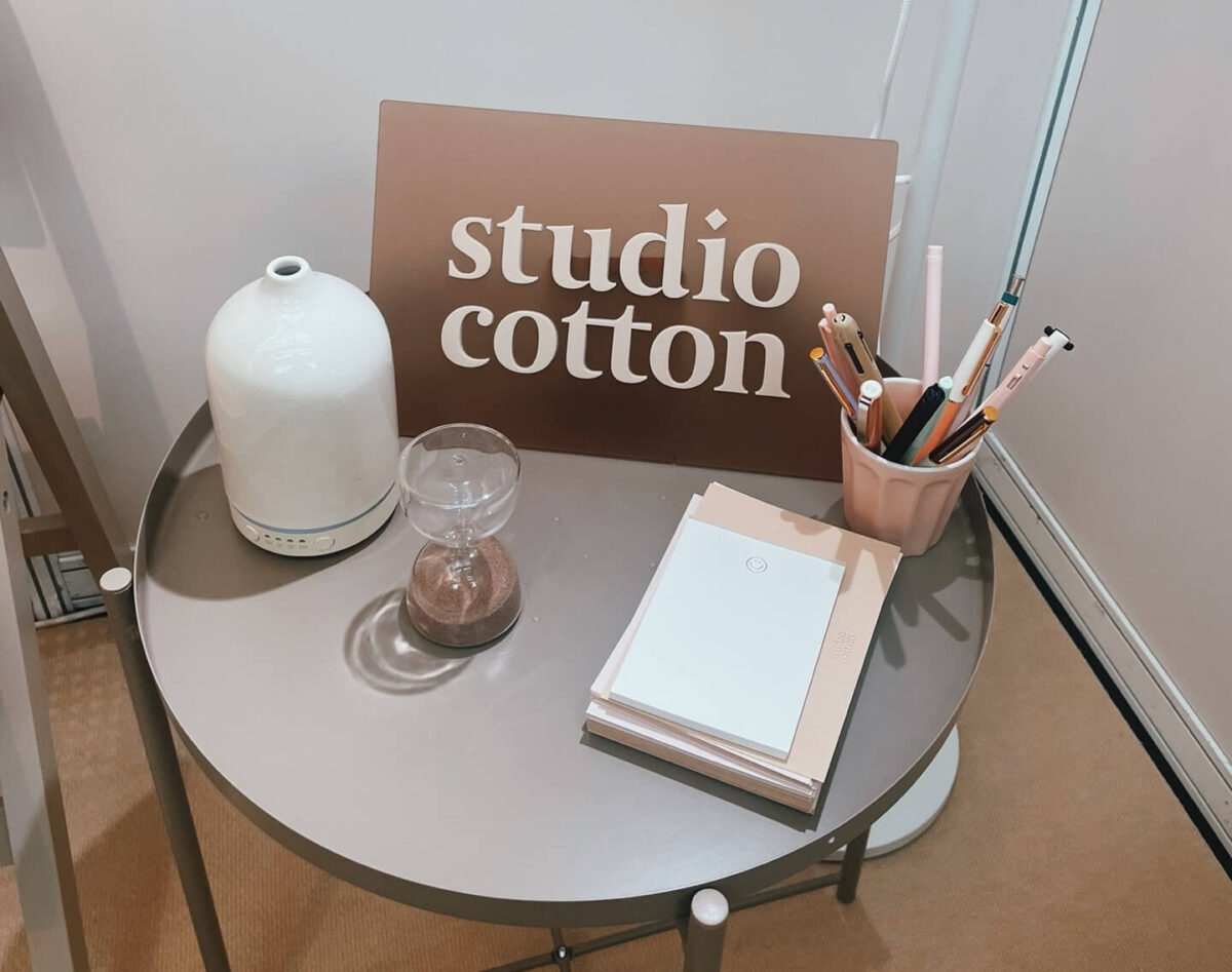 Circular side table with Studio Cotton logo, a pot with pens, notebook, egg timer, and scent diffuser